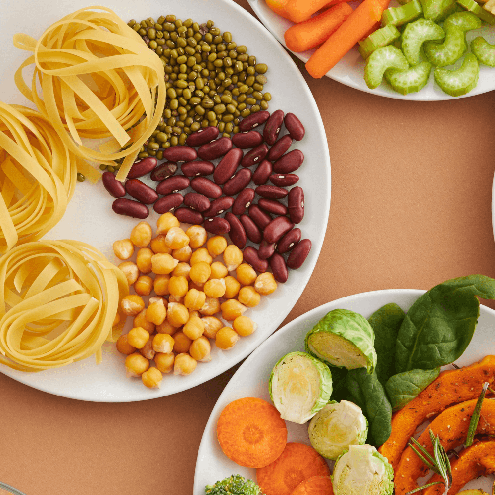 A vibrant mix of legumes, vegetables, nuts, and pasta arranged on white plates showcasing a balanced, healthy diet.